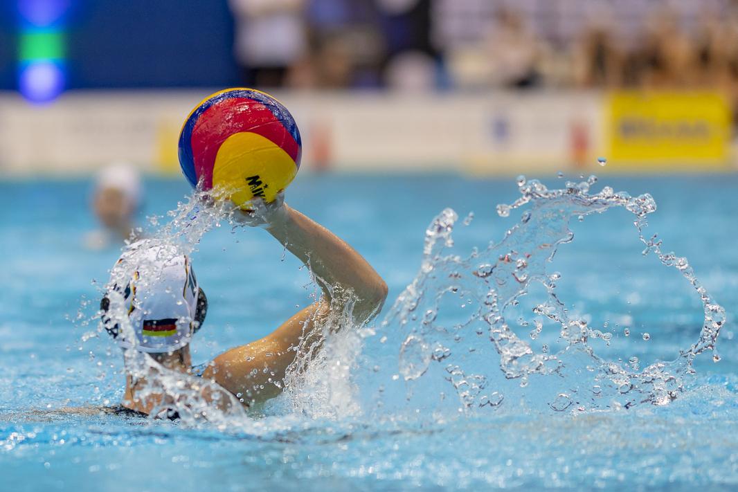 Eine Wasserballerin hält den Ball kur vor dem Pass in die Höhe.