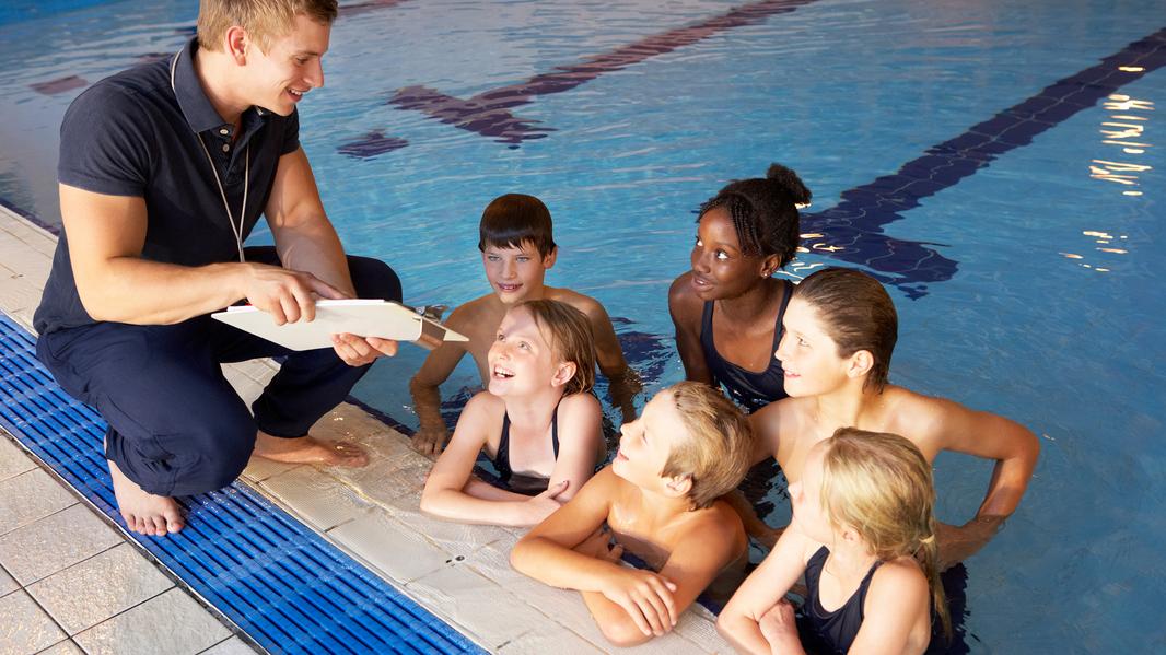 Ein Trainer erklärt Schwimmer*innen den Trainingsplan