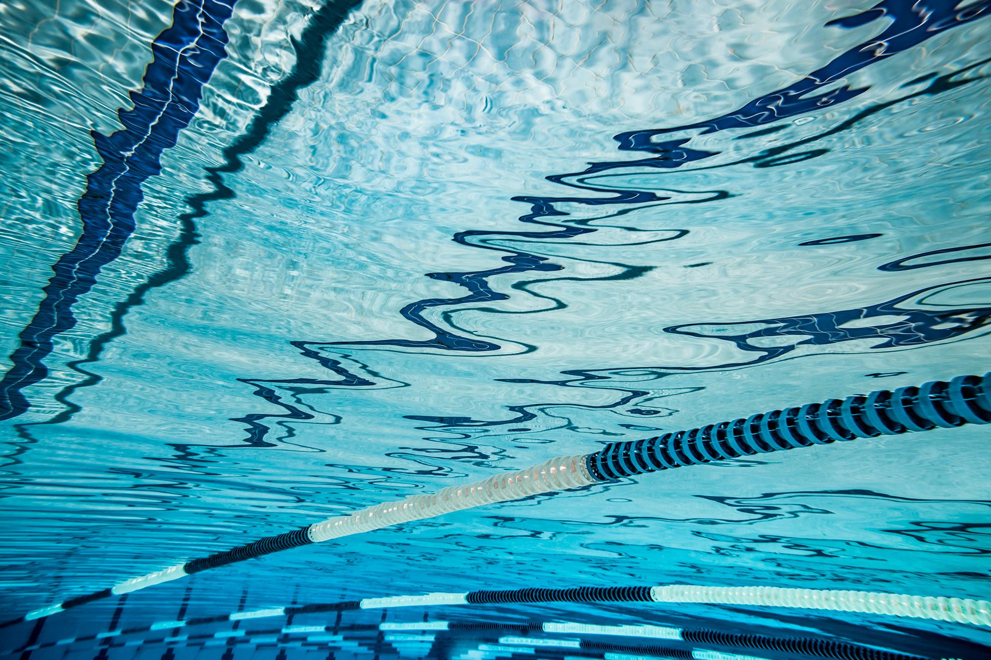 Unterwasseraufnahme eines Schwimmbeckens mit reflektierender Wasseroberfläche und Markierungen auf dem Boden.
